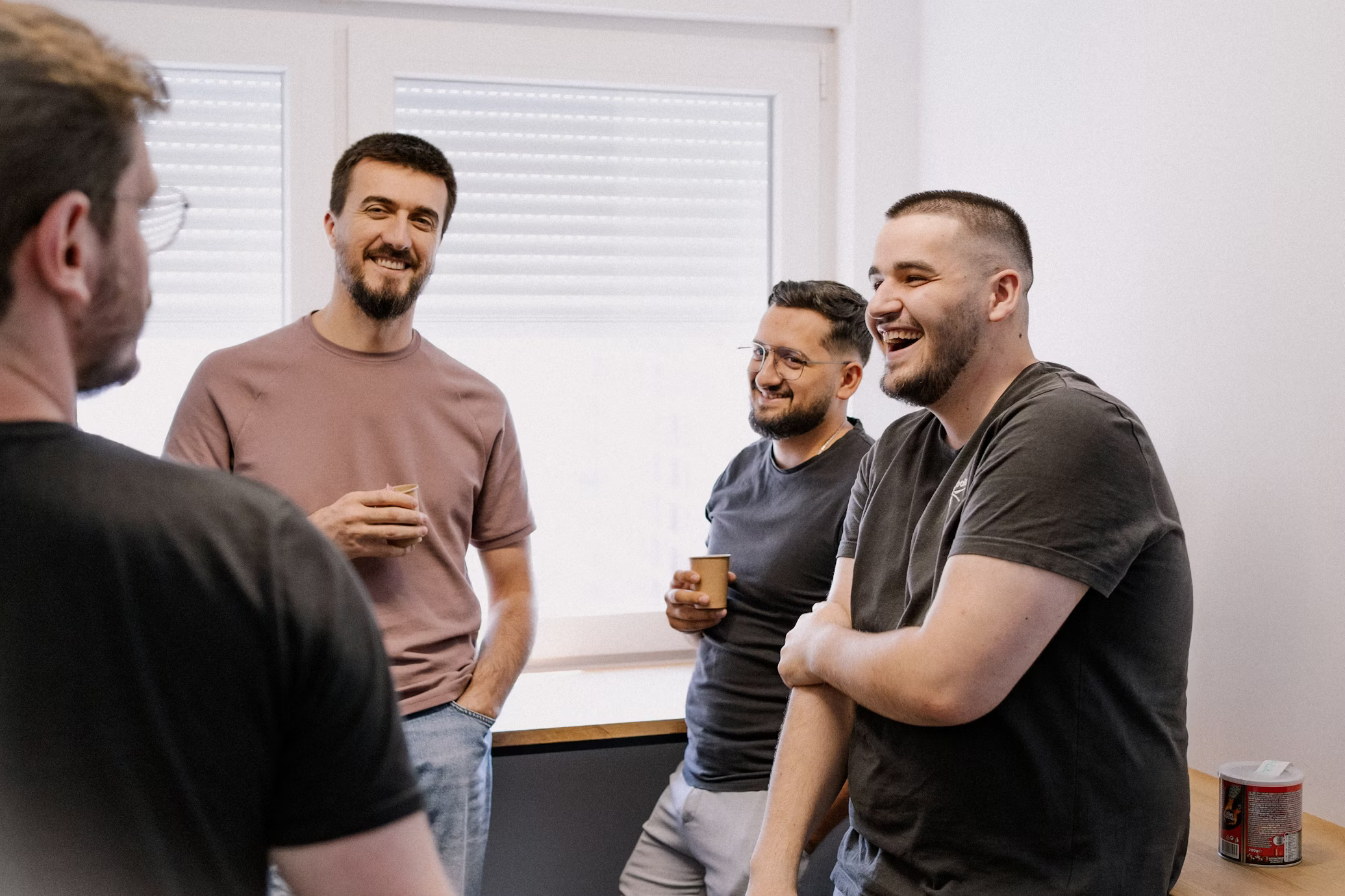 A team of four colleagues talking and laughing together in an office break area.